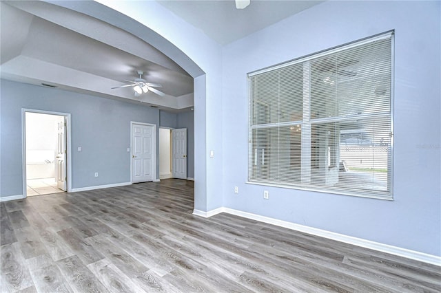 empty room with arched walkways, a ceiling fan, light wood-style flooring, and baseboards