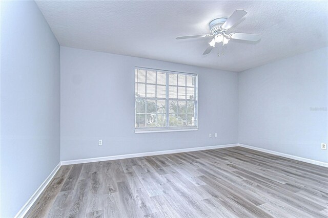 spare room featuring light wood finished floors, baseboards, and a textured ceiling