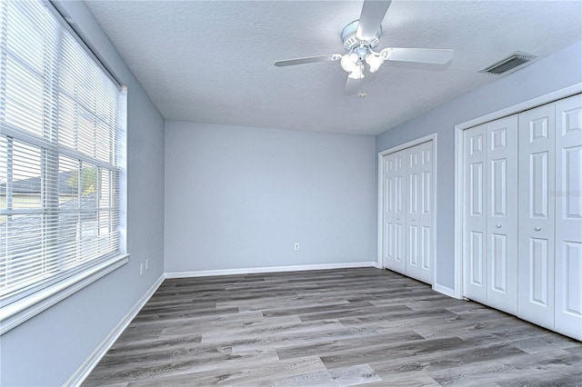 unfurnished bedroom featuring light wood-type flooring, a textured ceiling, visible vents, and two closets