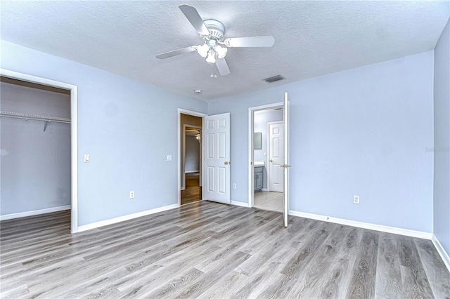 unfurnished bedroom with a textured ceiling, light wood-style flooring, visible vents, baseboards, and a closet