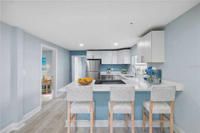 kitchen featuring white cabinetry, sink, kitchen peninsula, stainless steel fridge, and a kitchen bar