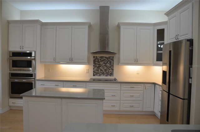 kitchen featuring white cabinets, light hardwood / wood-style flooring, wall chimney range hood, backsplash, and appliances with stainless steel finishes