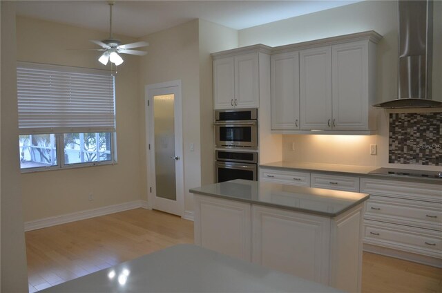 kitchen featuring a center island, ceiling fan, wall chimney range hood, white cabinetry, and stovetop