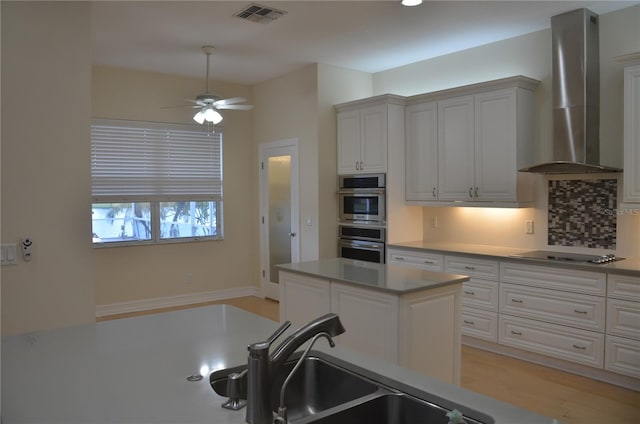 kitchen with white cabinetry, stovetop, wall chimney range hood, and double oven