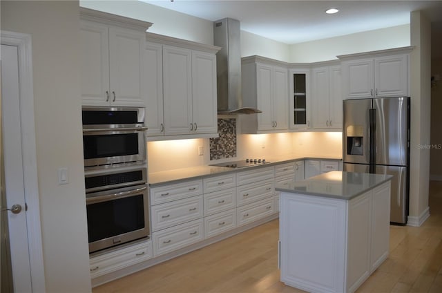 kitchen with white cabinets, wall chimney range hood, light hardwood / wood-style flooring, and appliances with stainless steel finishes