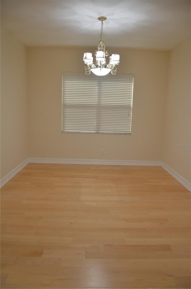 spare room featuring light wood-type flooring and a chandelier