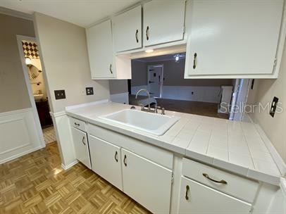 kitchen with tile countertops, white cabinetry, sink, and light parquet flooring