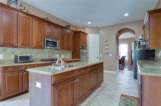 kitchen with tasteful backsplash, stainless steel appliances, a kitchen island with sink, and sink