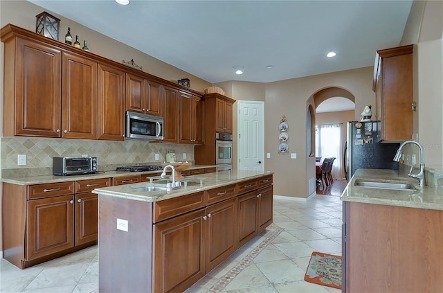 kitchen with decorative backsplash, appliances with stainless steel finishes, a center island with sink, and sink