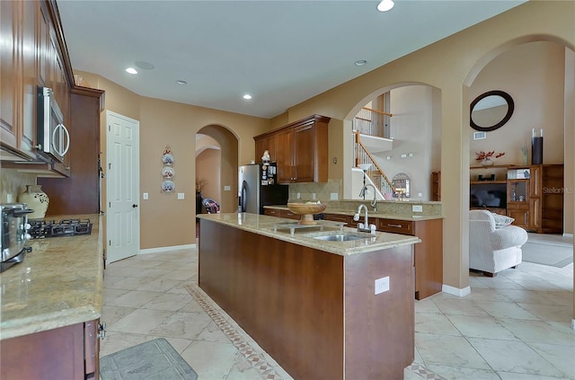 kitchen with light stone countertops, sink, backsplash, a kitchen island with sink, and appliances with stainless steel finishes