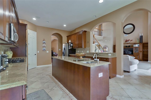 kitchen featuring appliances with stainless steel finishes, backsplash, light stone counters, a kitchen island with sink, and sink