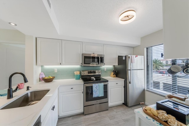 kitchen featuring white cabinetry, sink, stainless steel appliances, tasteful backsplash, and a textured ceiling