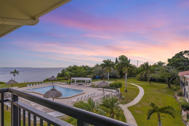 pool at dusk featuring a lawn, a patio area, and a water view