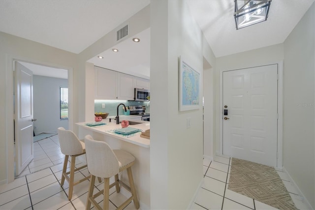 kitchen featuring a kitchen bar, stainless steel appliances, sink, white cabinets, and light tile patterned flooring