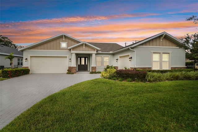 view of front of house featuring stone siding, decorative driveway, a lawn, and an attached garage