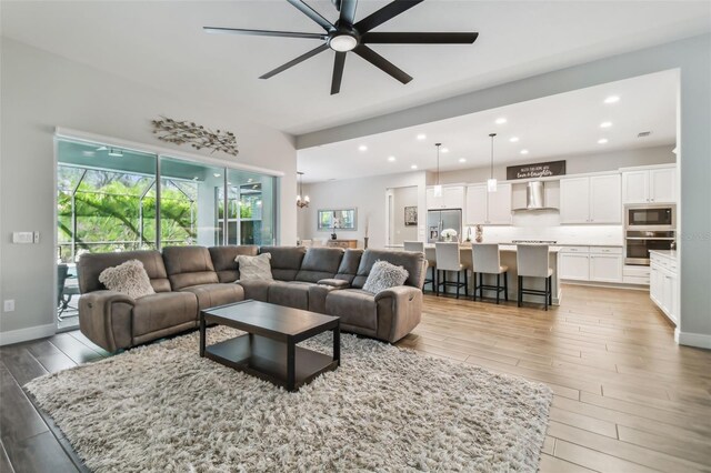 living room featuring light wood-style flooring, baseboards, a ceiling fan, and recessed lighting