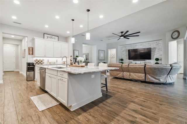 kitchen with white cabinets, an island with sink, decorative light fixtures, light stone countertops, and a sink