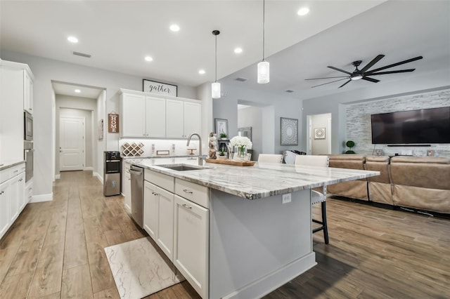 kitchen with a center island with sink, a breakfast bar area, white cabinetry, pendant lighting, and a sink