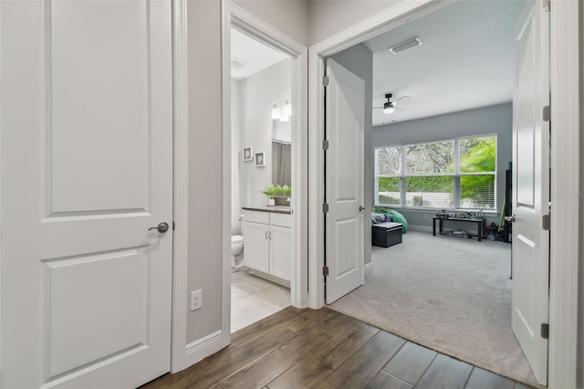 hallway with carpet flooring, visible vents, baseboards, and wood finished floors