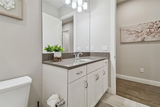 half bath with a notable chandelier, toilet, vanity, wood finished floors, and baseboards