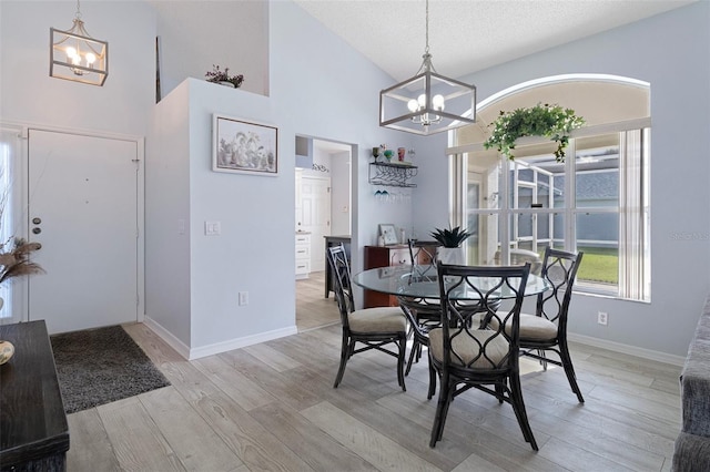 dining space with light hardwood / wood-style floors, a notable chandelier, high vaulted ceiling, and a textured ceiling