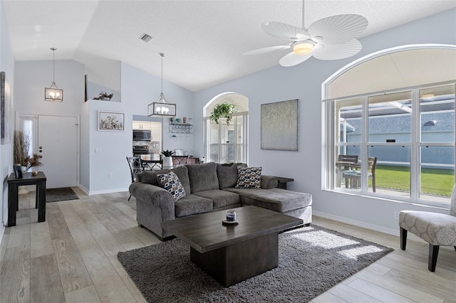 living room featuring a textured ceiling, lofted ceiling, light wood-type flooring, and ceiling fan with notable chandelier