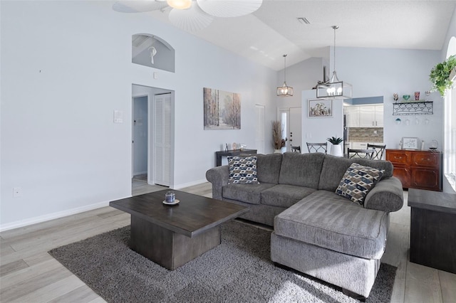 living room with light hardwood / wood-style floors, high vaulted ceiling, and ceiling fan with notable chandelier