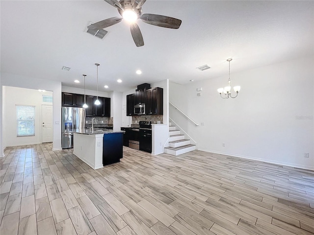 kitchen featuring light hardwood / wood-style floors, an island with sink, backsplash, appliances with stainless steel finishes, and ceiling fan with notable chandelier