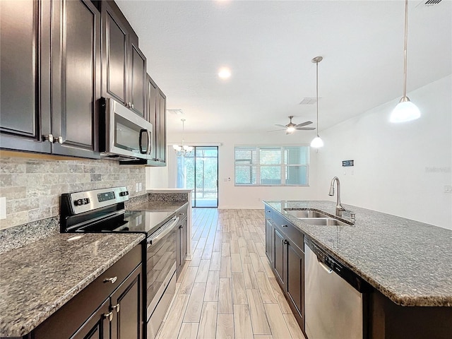 kitchen with dark brown cabinets, a center island with sink, appliances with stainless steel finishes, sink, and decorative light fixtures