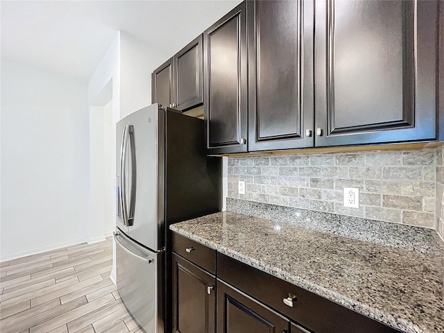 kitchen featuring backsplash, light stone countertops, dark brown cabinetry, and light wood-type flooring