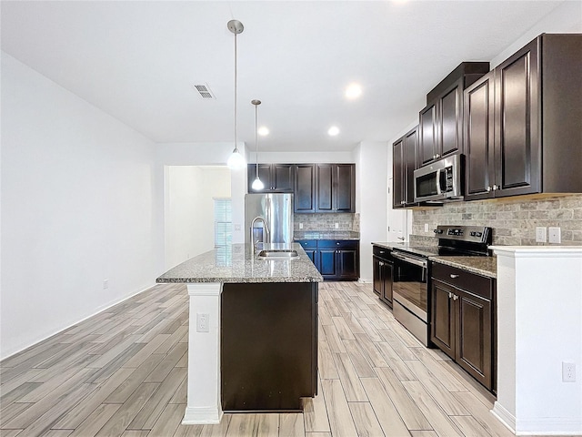 kitchen featuring appliances with stainless steel finishes, sink, decorative light fixtures, light hardwood / wood-style flooring, and a kitchen island with sink