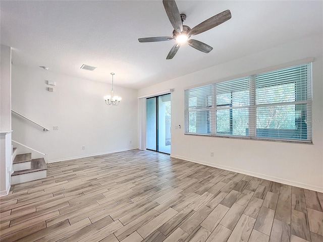 empty room with light hardwood / wood-style flooring, a textured ceiling, ceiling fan with notable chandelier, and a wealth of natural light