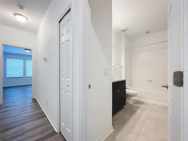 full bathroom with wood-type flooring, a textured ceiling, toilet, vanity, and tiled shower / bath combo