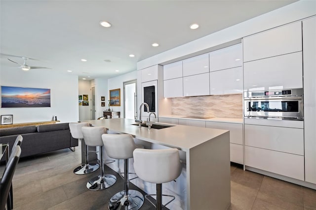 kitchen featuring sink, a kitchen breakfast bar, backsplash, an island with sink, and oven