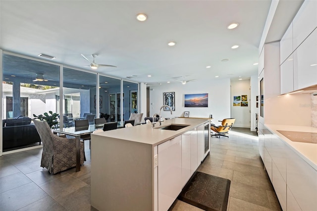 kitchen with black electric cooktop, a center island with sink, sink, and white cabinetry