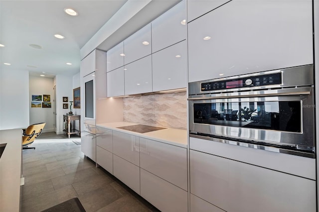 kitchen with black electric stovetop, white cabinets, oven, dark tile patterned floors, and backsplash