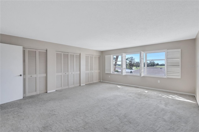 unfurnished bedroom featuring a textured ceiling, two closets, and carpet floors