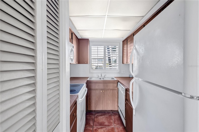 kitchen with dark tile patterned floors, backsplash, sink, and white appliances