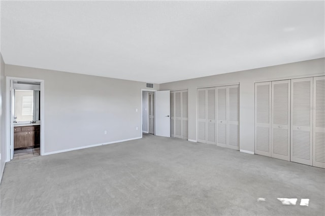 unfurnished bedroom with connected bathroom, light carpet, and multiple closets