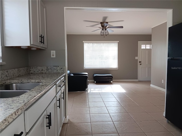 kitchen with light stone countertops, black fridge, ceiling fan, white cabinets, and light tile patterned floors