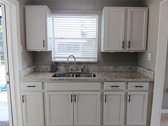 kitchen with light stone counters, sink, and white cabinets