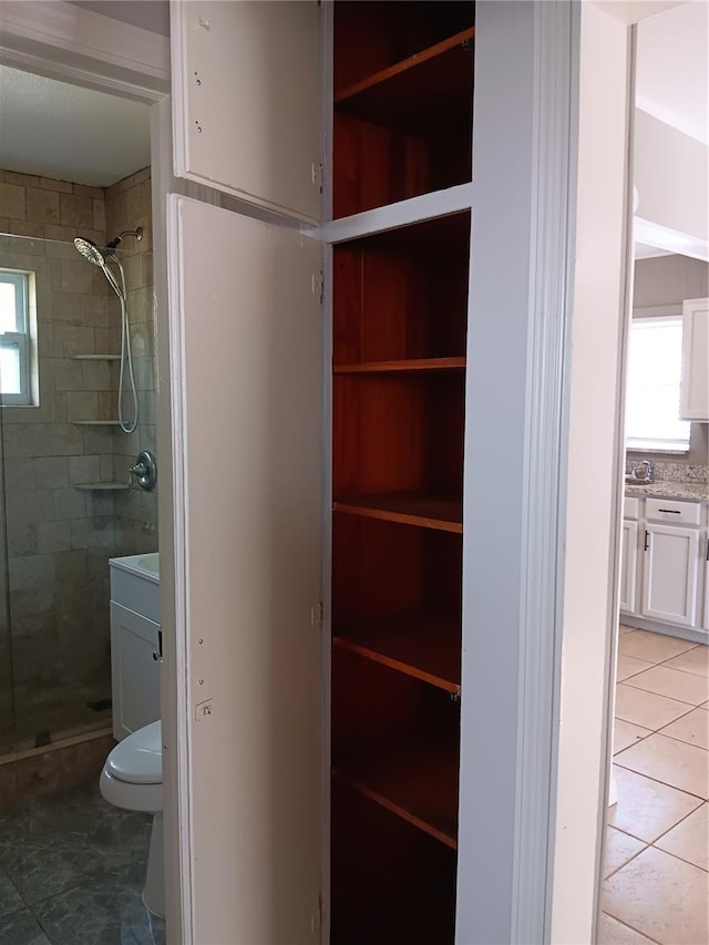 bathroom with toilet, vanity, tile patterned floors, and tiled shower