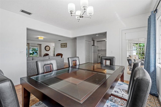 dining room featuring hardwood / wood-style flooring, a wealth of natural light, a textured ceiling, and a chandelier