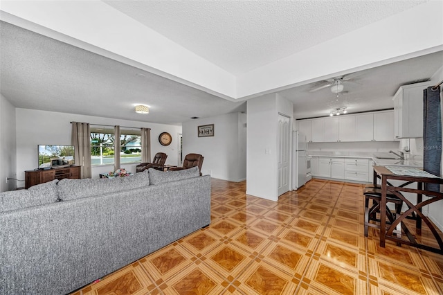 living room featuring sink, a textured ceiling, and ceiling fan