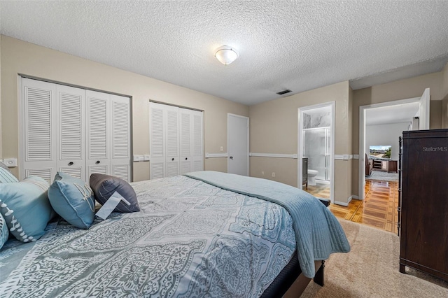 bedroom featuring multiple closets, light colored carpet, a textured ceiling, and connected bathroom