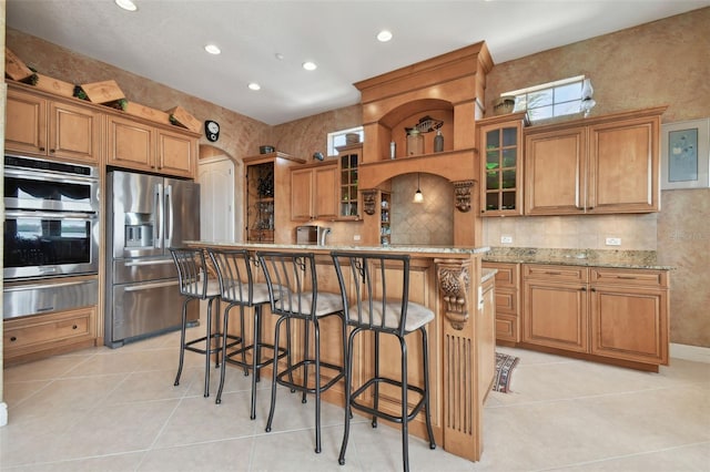 kitchen featuring light stone countertops, stainless steel appliances, a kitchen breakfast bar, a kitchen island with sink, and light tile patterned floors