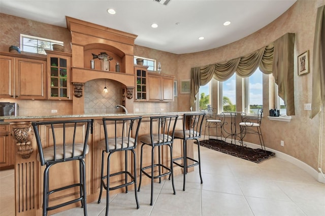 kitchen featuring a kitchen bar, light tile patterned flooring, backsplash, and a healthy amount of sunlight