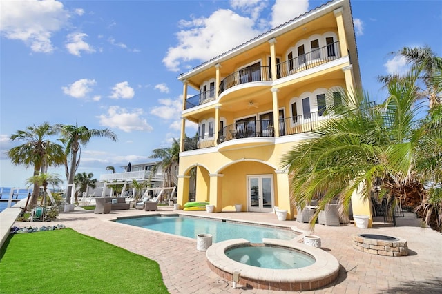 back of house with a balcony, french doors, an outdoor fire pit, a patio, and a pool with hot tub