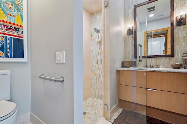 bathroom featuring toilet, tiled shower, and vanity