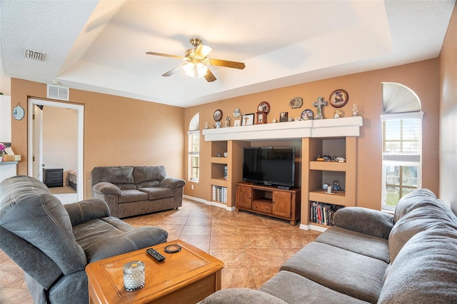 living room featuring ceiling fan, a tray ceiling, a textured ceiling, and light tile patterned floors